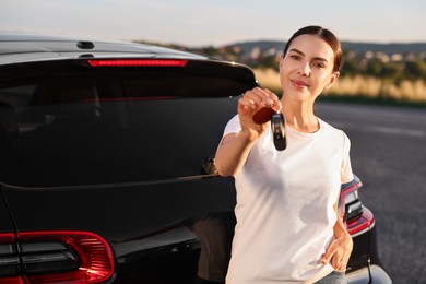 Beautiful young woman with key near her new car outdoors