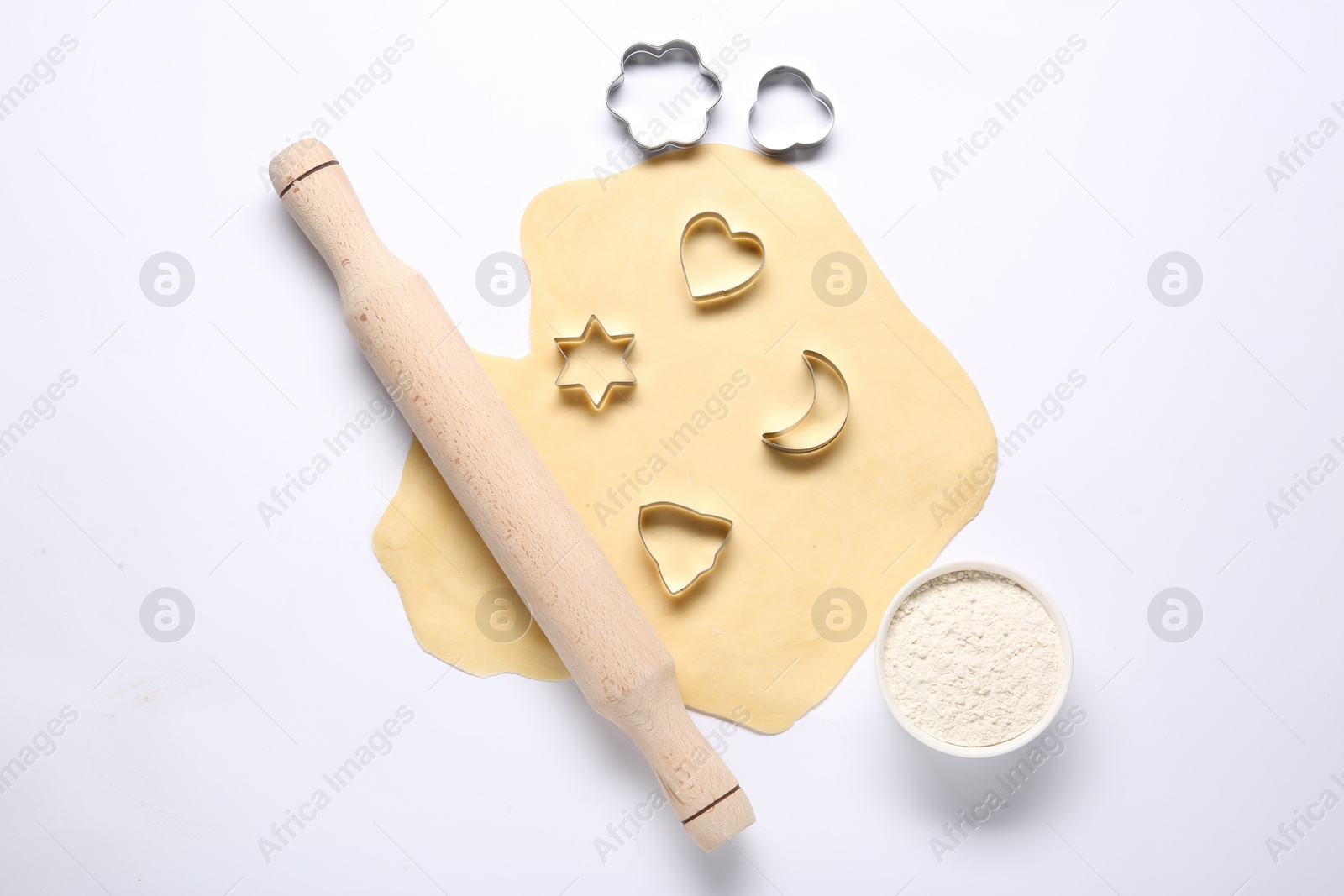 Photo of Raw dough, wooden rolling pin, flour and cookie cutters isolated on white, top view