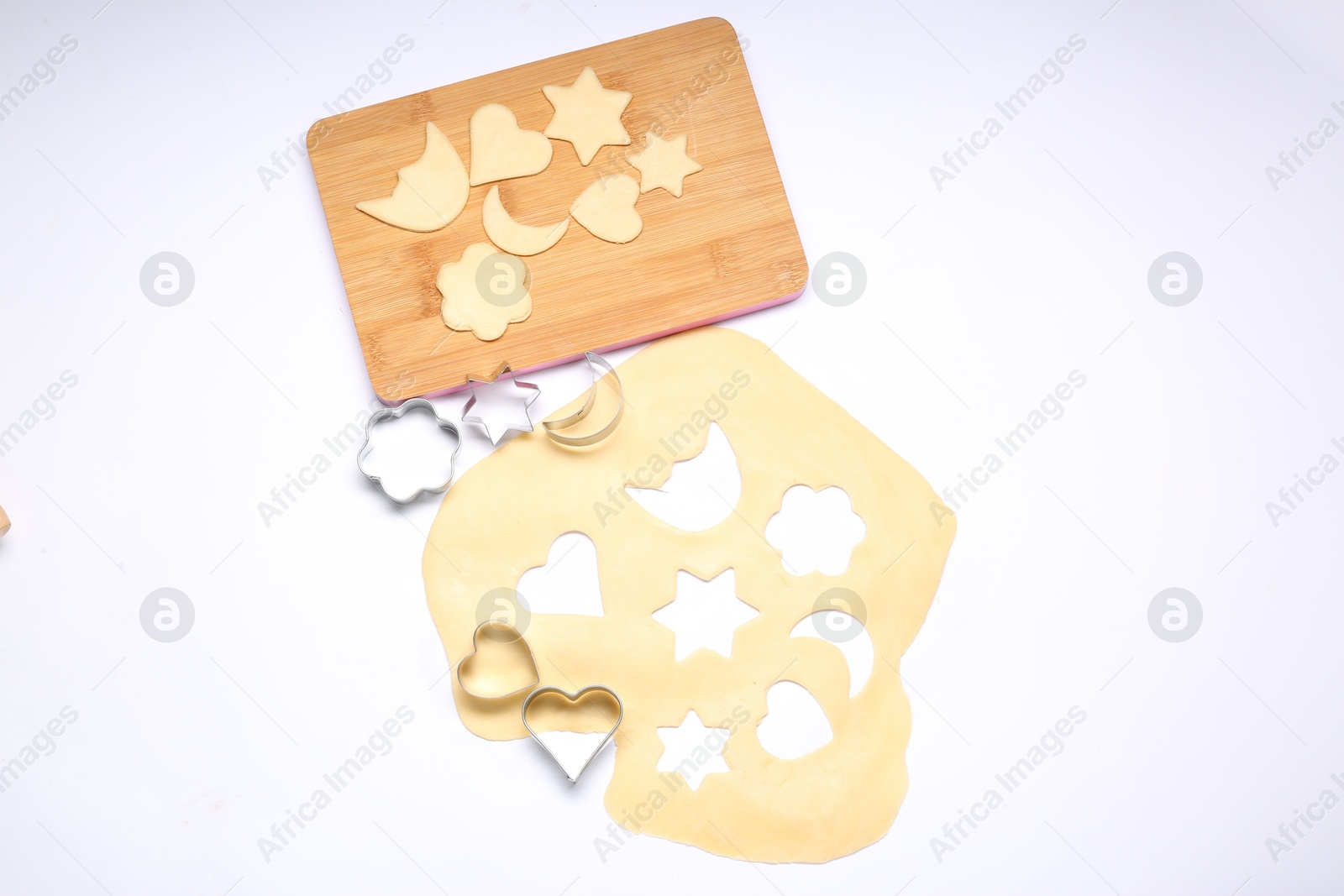 Photo of Raw dough, wooden board and cookie cutters isolated on white, top view