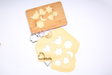 Raw dough, wooden board and cookie cutters isolated on white, top view