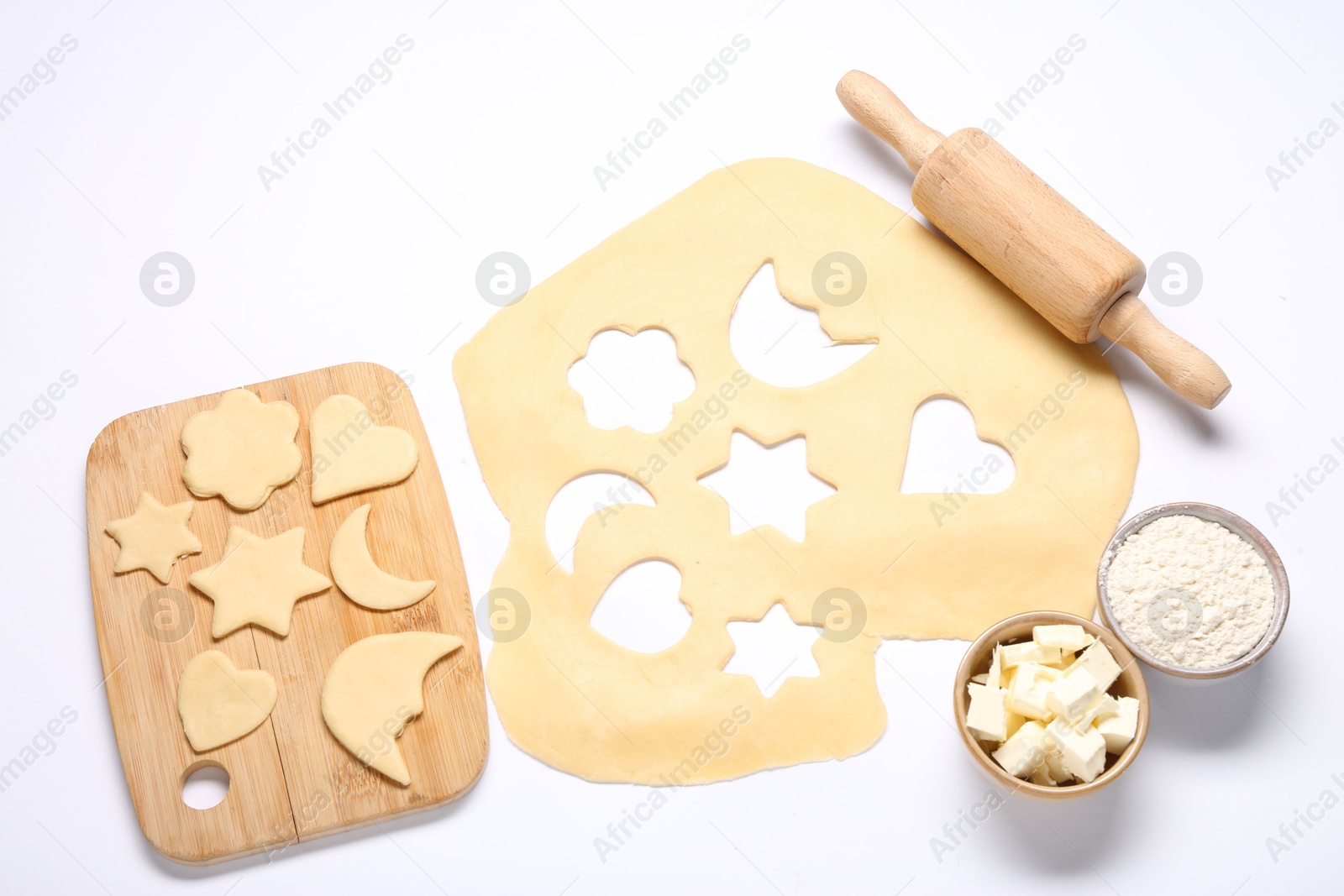 Photo of Raw dough, uncooked cookies, flour, butter, rolling pin and board isolated on white, above view