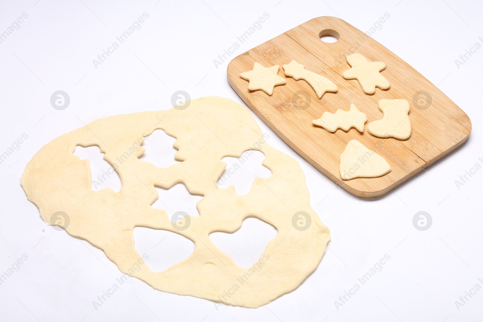 Photo of Raw dough, uncooked cookies and wooden board isolated on white