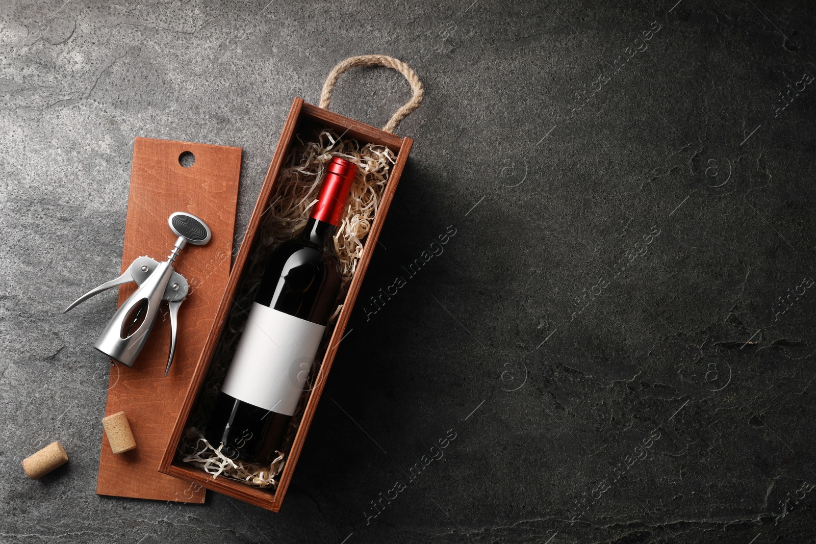Photo of Bottle of wine in wooden box, corks and corkscrew on dark textured table, flat lay. Space for text