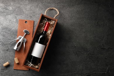 Photo of Bottle of wine in wooden box, corks and corkscrew on dark textured table, flat lay. Space for text