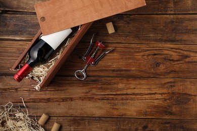 Photo of Box with wine bottle, corkscrew and corks on wooden table, flat lay. Space for text