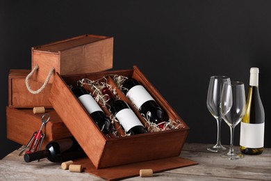 Photo of Box with wine bottles and glasses on wooden table against black background