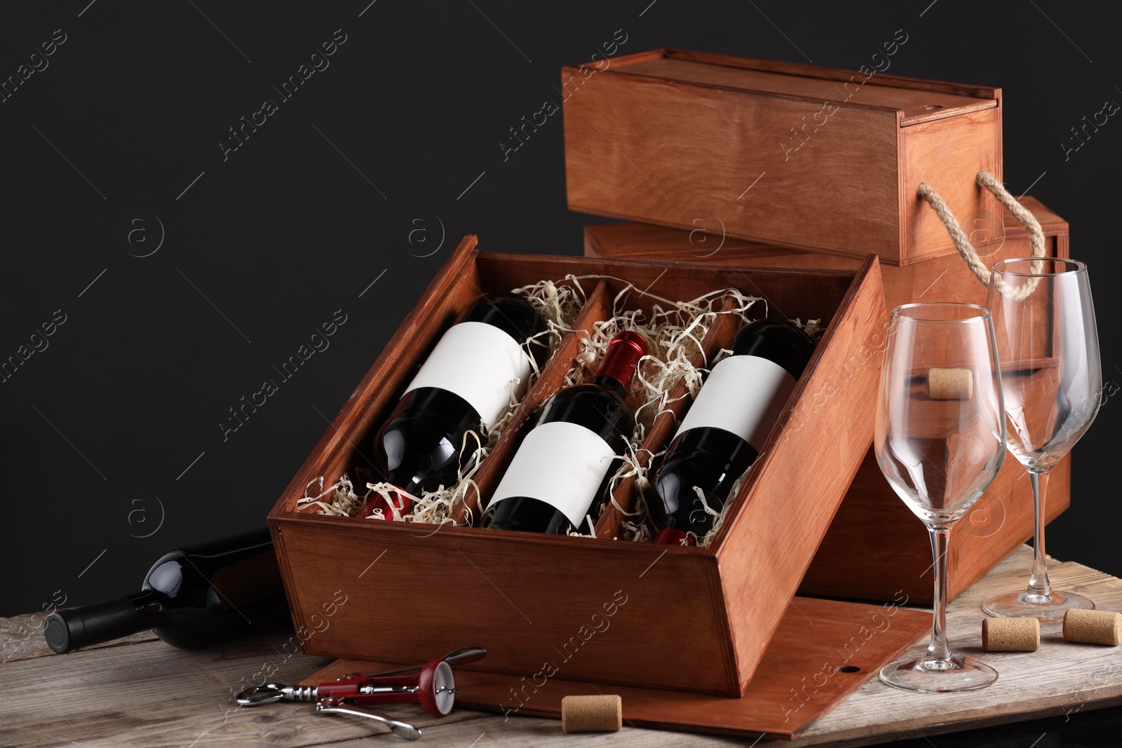 Photo of Box with wine bottles and glasses on wooden table against black background