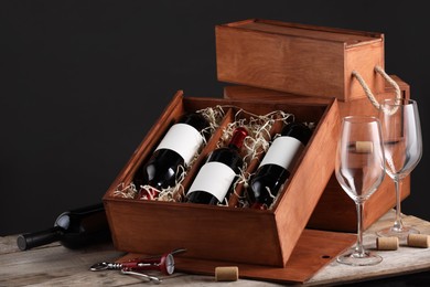 Box with wine bottles and glasses on wooden table against black background