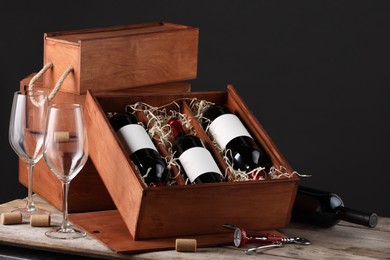 Photo of Box with wine bottles and glasses on wooden table against black background