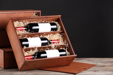 Photo of Box with wine bottles on wooden table against black background. Space for text