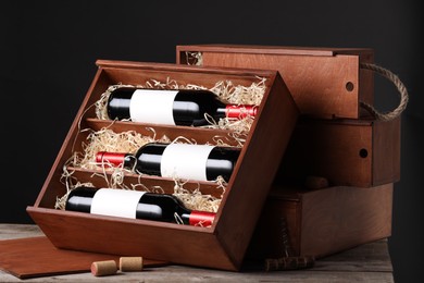 Box with wine bottles on wooden table against black background