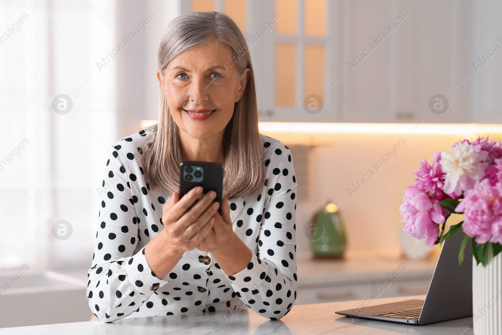 Photo of Senior woman using mobile phone at white table indoors