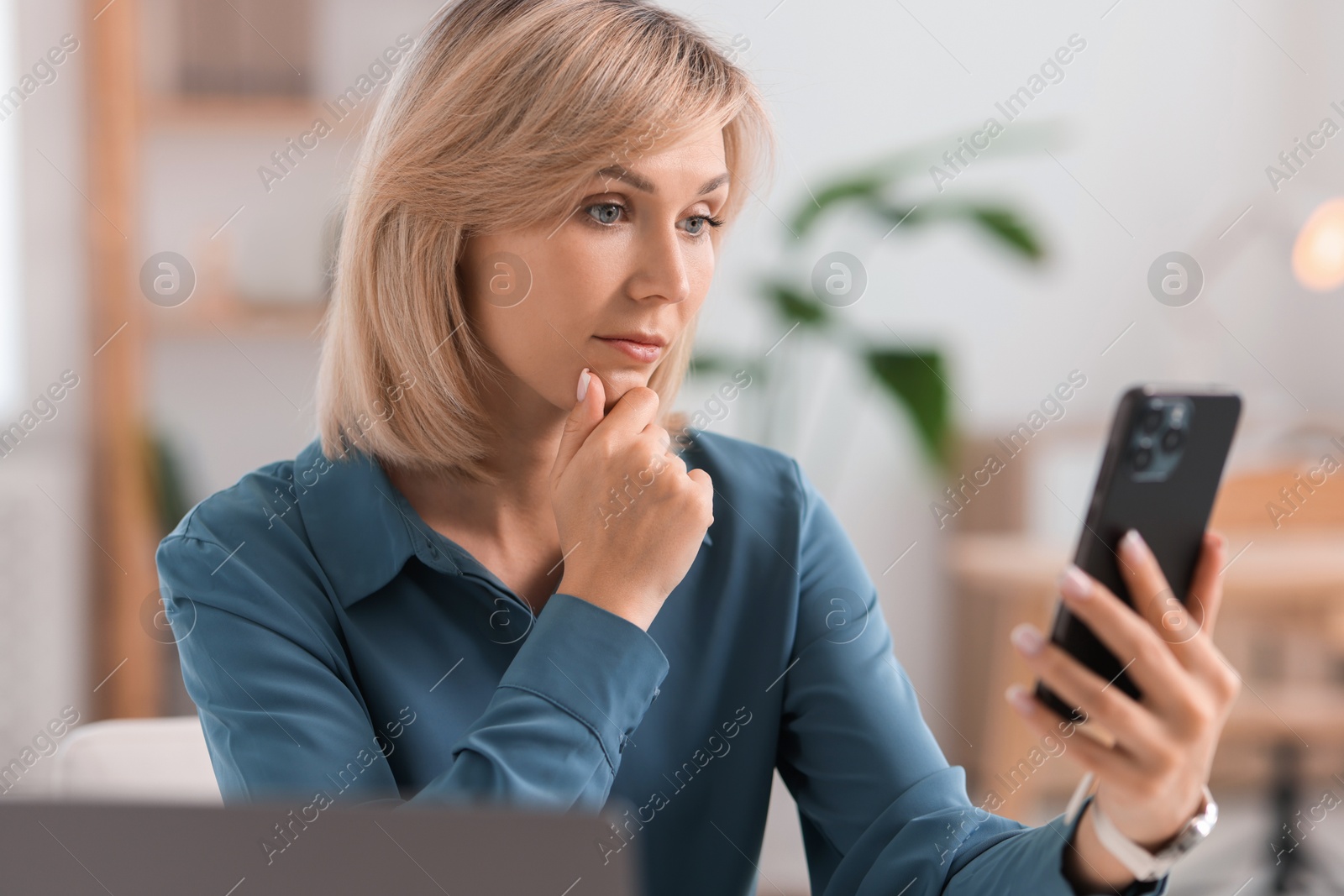 Photo of Woman using modern mobile phone at table indoors