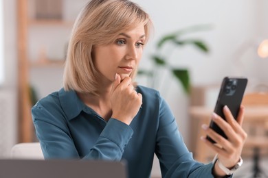 Woman using modern mobile phone at table indoors