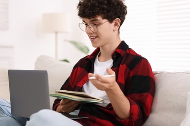 Teenager with notebooks and pen working on laptop at home. Remote job