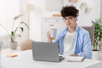 Teenager with cup of drink working on laptop at home. Remote job