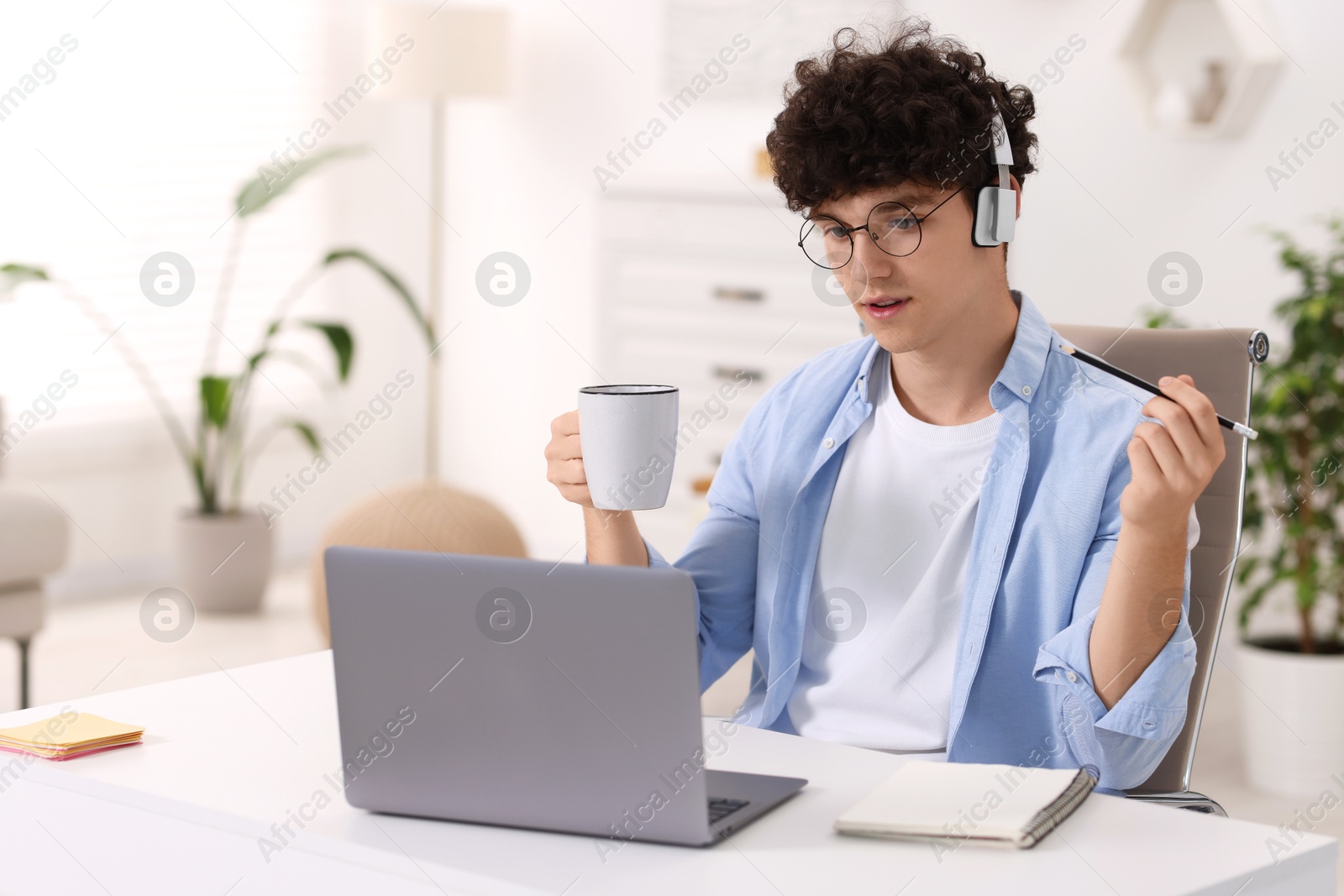 Photo of Teenager with cup of drink and pencil working on laptop at home. Remote job