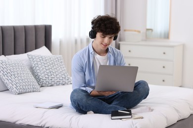 Photo of Teenager in headphones working with laptop on bed at home. Remote job