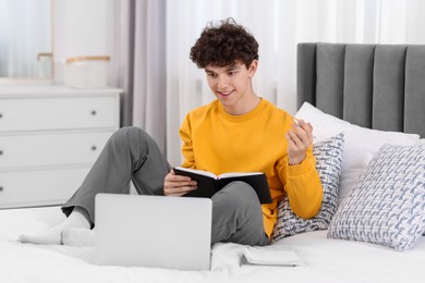 Teenager with pen and notebook working on laptop at home. Remote job