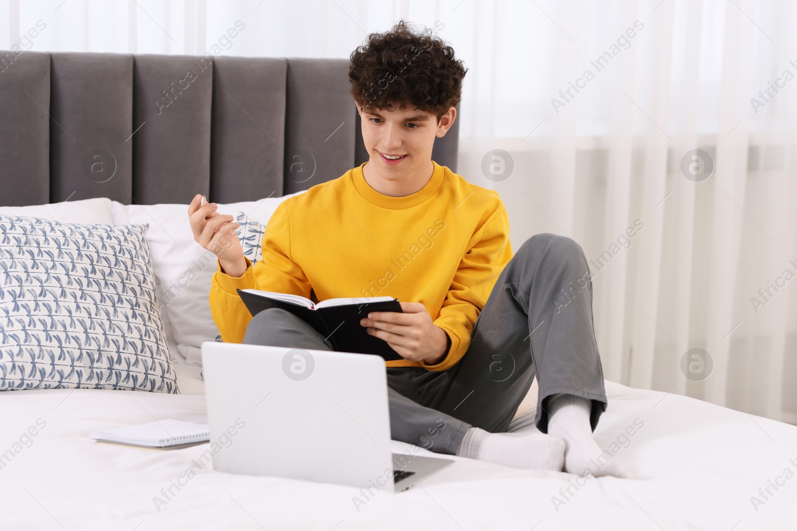 Photo of Teenager with pen and notebook working on laptop at home. Remote job