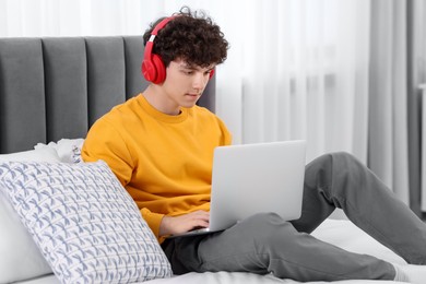 Teenager in headphones working with laptop on bed at home. Remote job