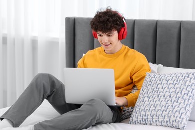 Teenager in headphones working with laptop on bed at home. Remote job