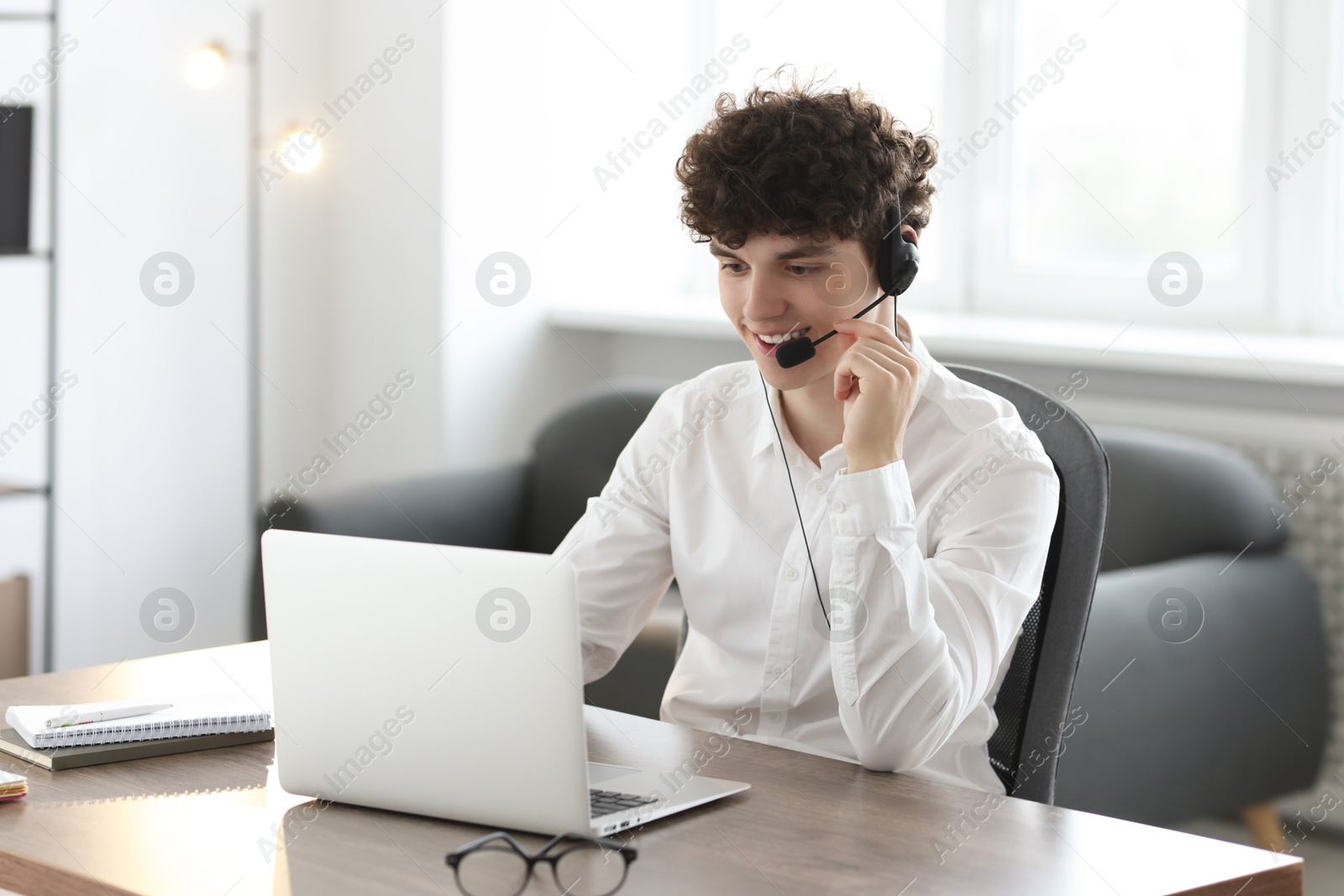 Photo of Teenager in headset working with laptop at table indoors. Remote job