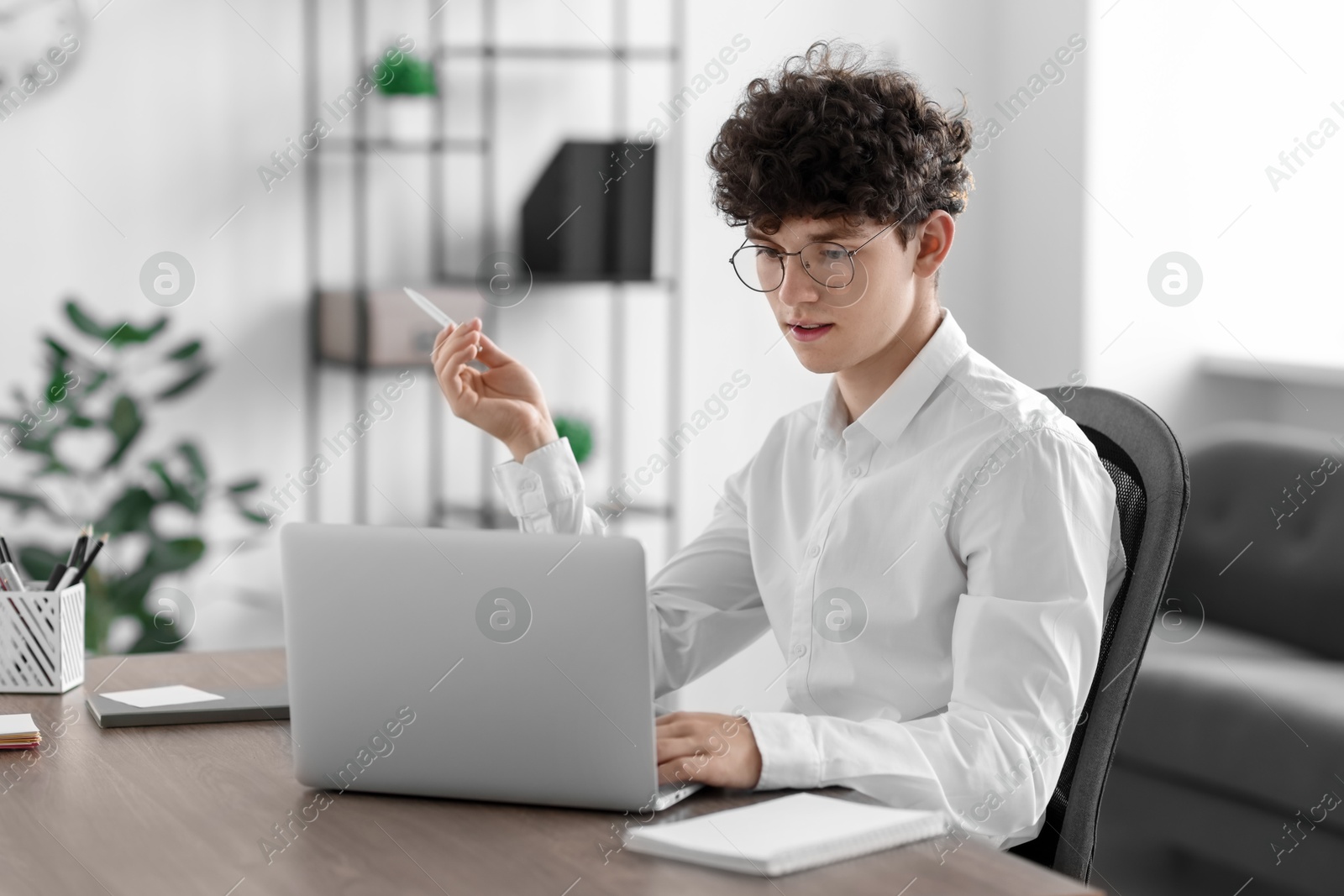 Photo of Teenager with pen working on laptop at table indoors. Remote job