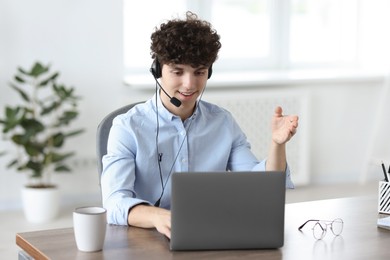 Photo of Teenager in headset having video chat via laptop at table indoors. Remote work