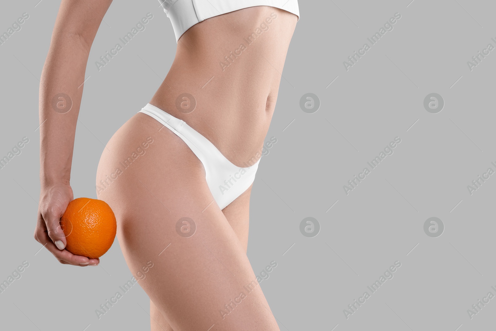 Photo of Woman in underwear with orange on light grey background, closeup. Cellulite problem