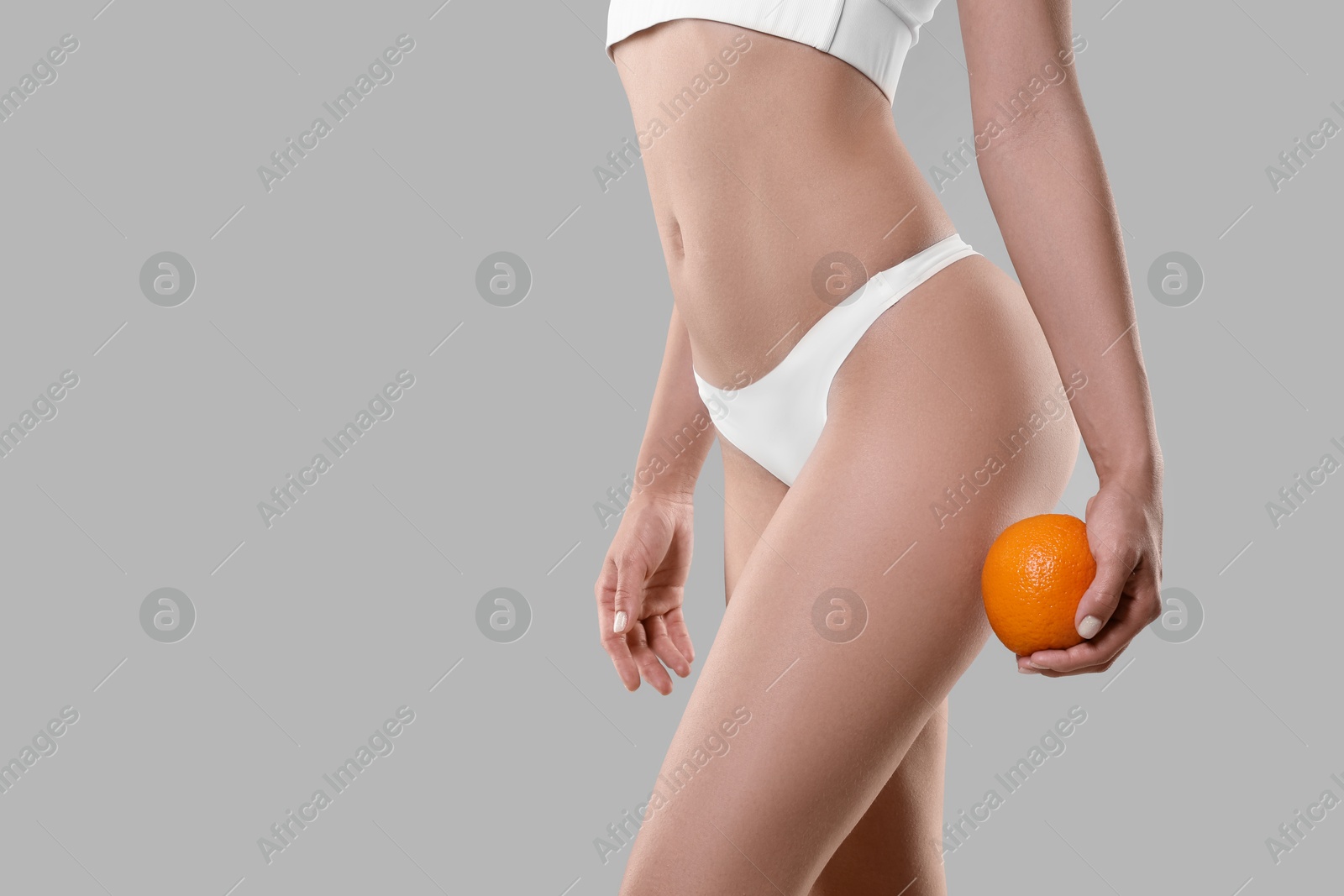 Photo of Woman in underwear with orange on light grey background, closeup. Cellulite problem