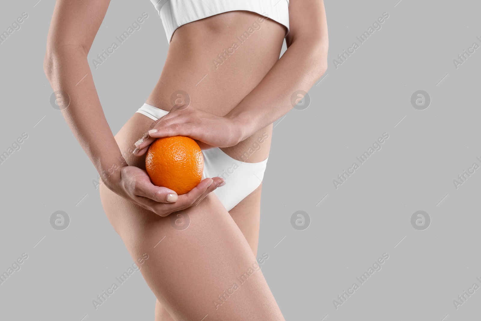 Photo of Woman in underwear with orange on light grey background, closeup. Cellulite problem