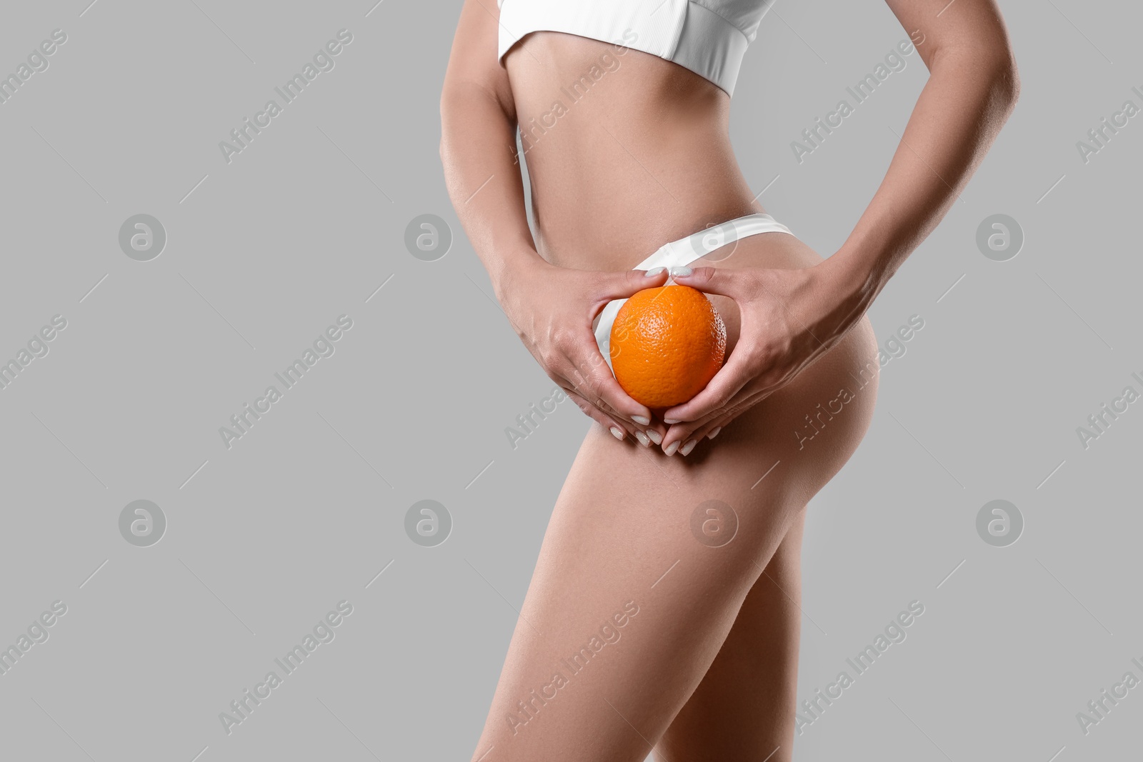 Photo of Woman in underwear with orange on light grey background, closeup. Cellulite problem