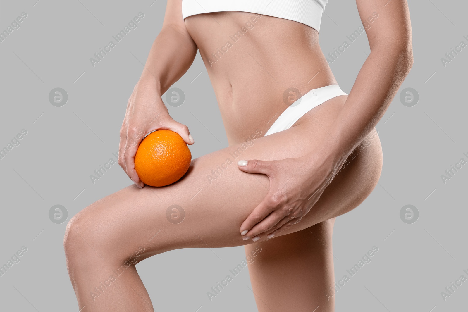 Photo of Woman in underwear with orange on light grey background, closeup. Cellulite problem