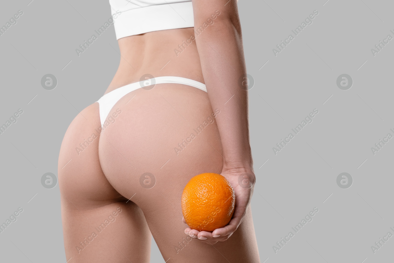 Photo of Woman in underwear with orange on light grey background, closeup. Cellulite problem
