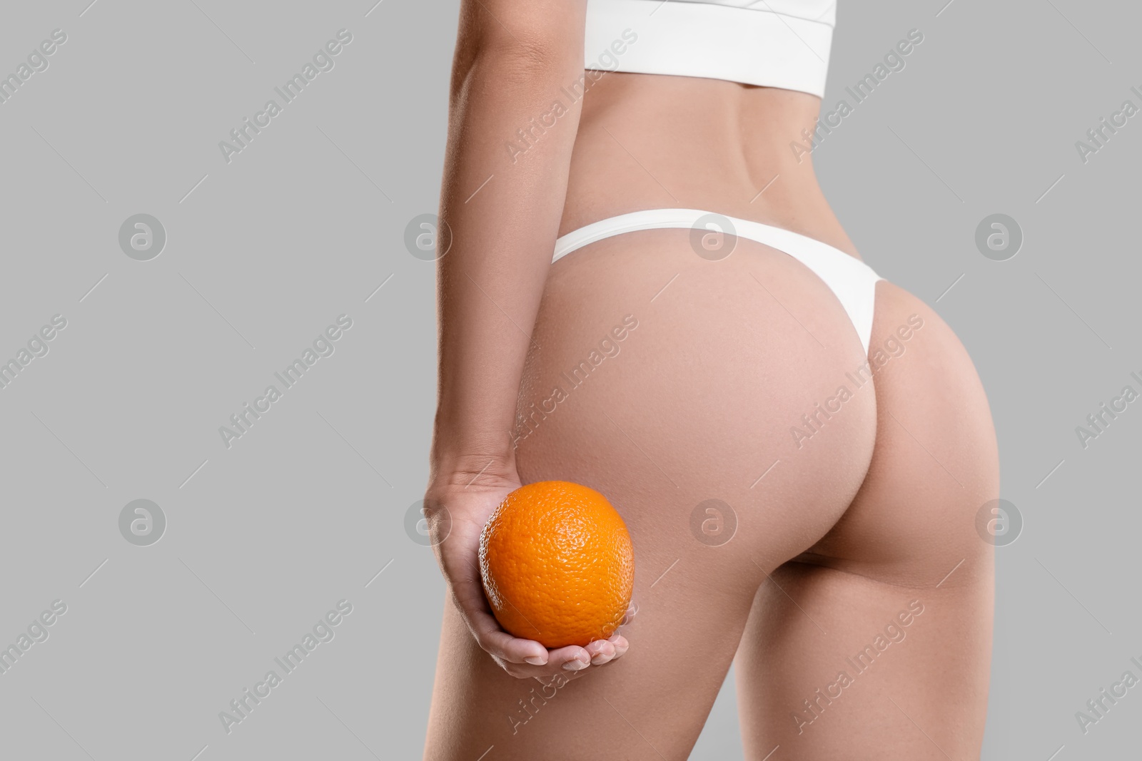 Photo of Woman in underwear with orange on light grey background, closeup. Cellulite problem