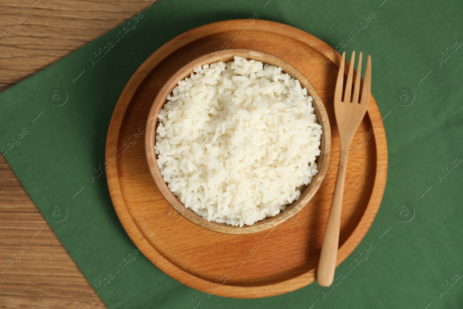 Photo of Delicious boiled rice in bowl and fork on wooden table, top view