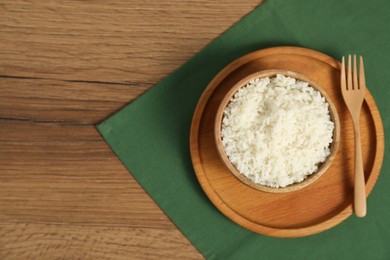 Photo of Delicious boiled rice in bowl and fork on wooden table, top view. Space for text