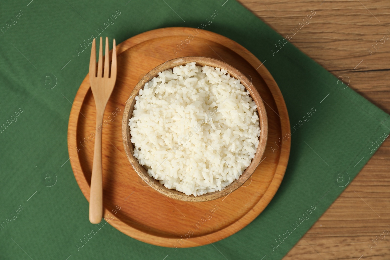 Photo of Delicious boiled rice in bowl and fork on wooden table, top view