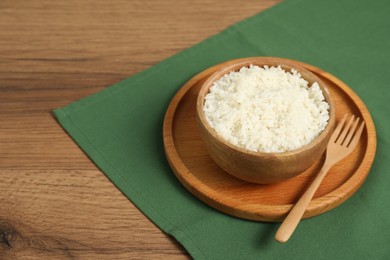 Photo of Delicious boiled rice in bowl and fork on wooden table