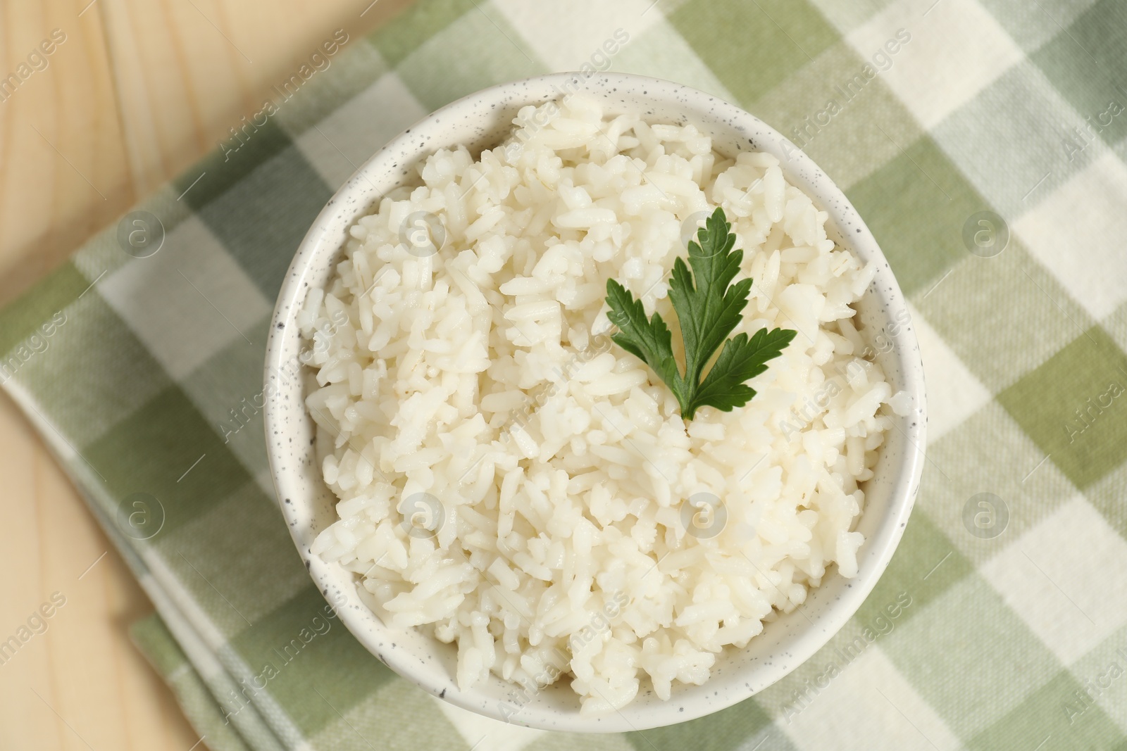 Photo of Delicious boiled rice in bowl and parsley on wooden table, top view