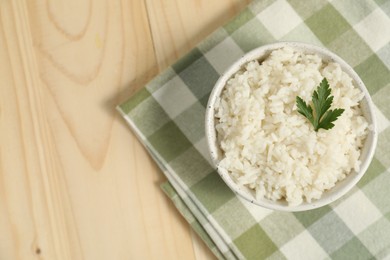 Photo of Delicious boiled rice in bowl and parsley on wooden table, top view. Space for text