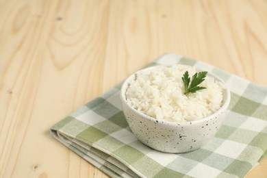 Photo of Delicious boiled rice in bowl and parsley on wooden table. Space for text