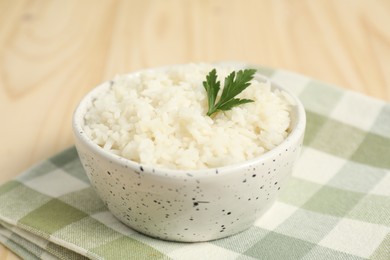 Photo of Delicious boiled rice in bowl and parsley on table, closeup