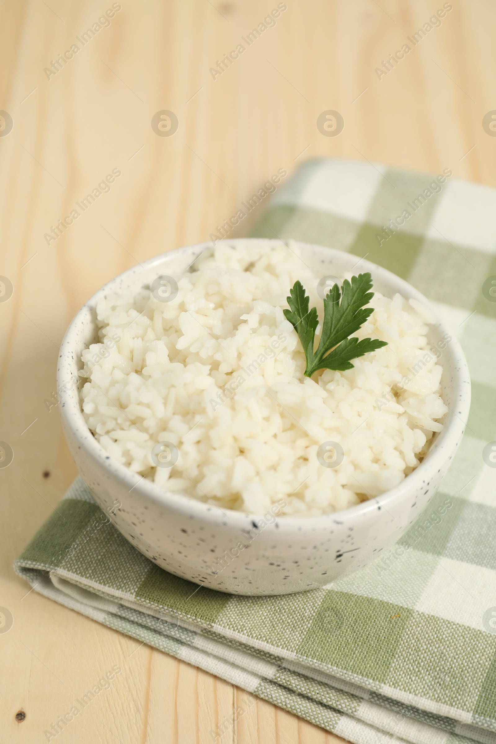 Photo of Delicious boiled rice in bowl and parsley on wooden table