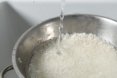 Photo of Pouring water into bowl with rice in sink, closeup