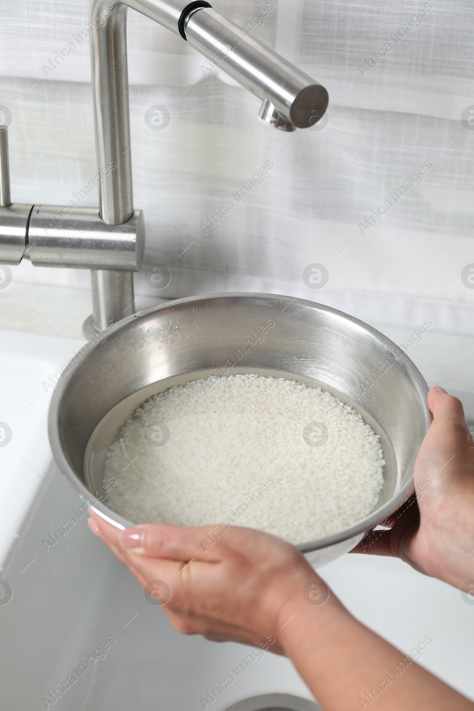 Photo of Woman holding bowl with rice and water above sink, closeup