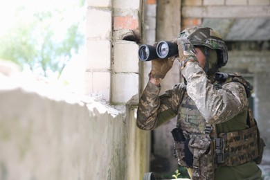 Photo of Military mission. Soldier in uniform with binoculars inside abandoned building, space for text