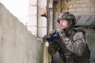 Military mission. Soldier in uniform with binoculars inside abandoned building, space for text