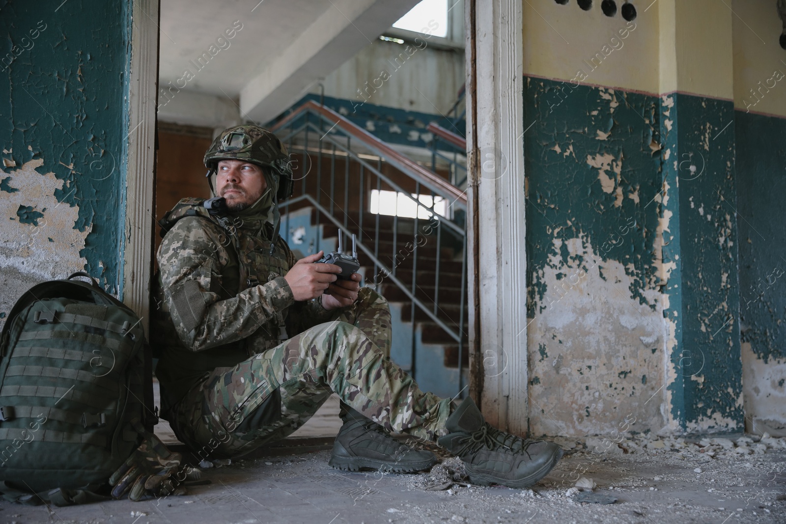 Photo of Military mission. Soldier in uniform with drone controller inside abandoned building